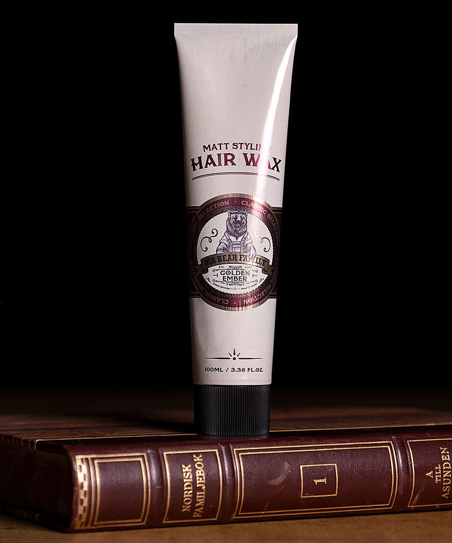 Tubo de MR BEAR FAMILY Hair Wax Golden Ember sobre un libro con fondo negro