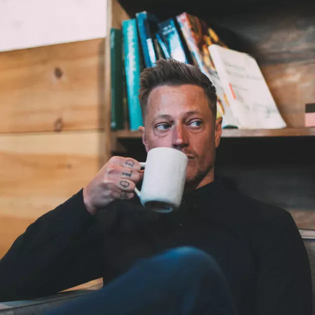 Hombre rubio bebiendo de una taza, peinado con SHEAR REVIVAL Northern Lights
