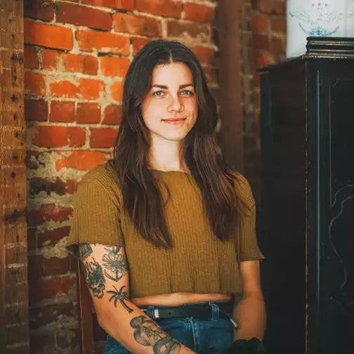 Mujer morena con tatuajes ante una pared de ladrillo, imagen de SHEAR REVIVAL Progress