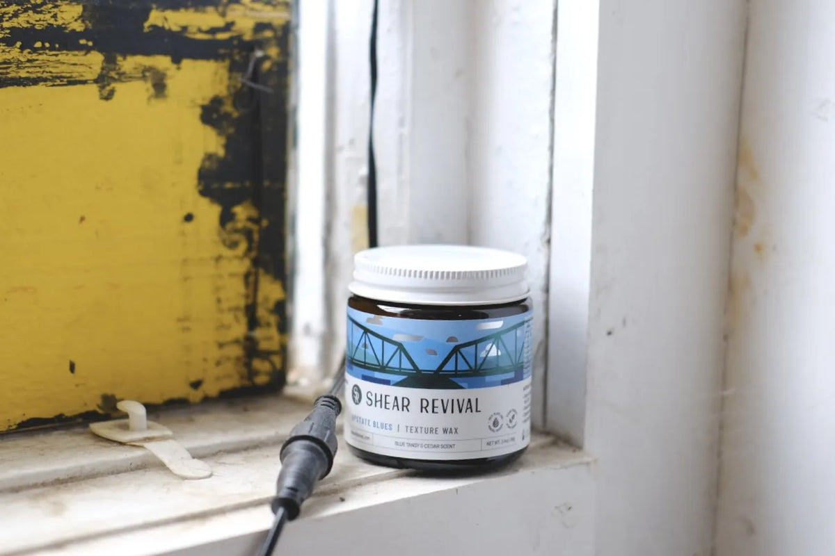 Tarro de SHEAR REVIVAL Upstate Blues Texture Wax junto a una ventana