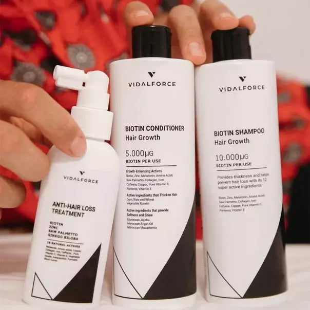 Manos sosteniendo el spray, el acondicionador y el champú de biotina de VIDALFORCE