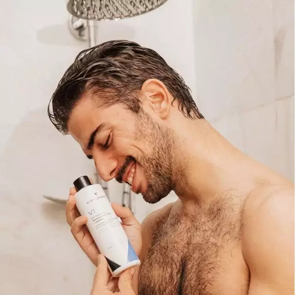 Hombre sonriendo en la ducha abrazando la botella de VIDALFORCE champú V1