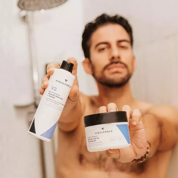 Hombre en la ducha mostrando el champú V2 y un tarro de VIDALFORCE