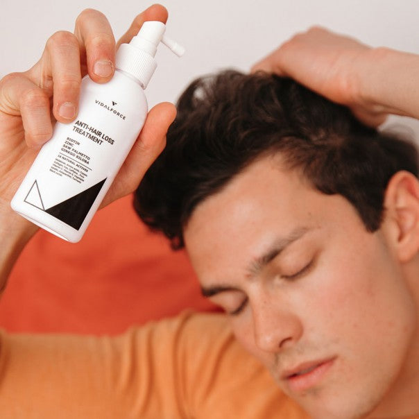 Hombre con los ojos cerrados sosteniendo el spray de tratamiento VIDALFORCE junto a su cabeza