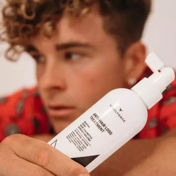 Hombre de pelo rizado sosteniendo el spray de VIDALFORCE tónico tratamiento