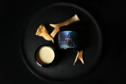 Pomada Elemental Alchemist abierta junto a un cuerno sobre un plato oscuro