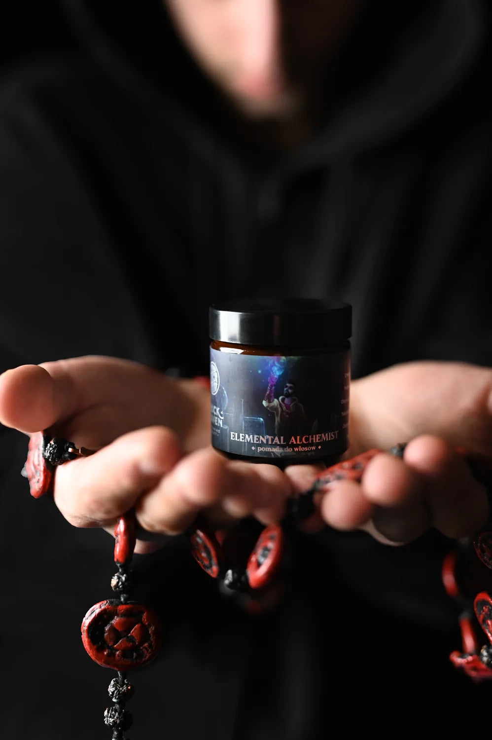Manos ofreciendo el bote de Elemental Alchemist con un collar de cuentas rojas
